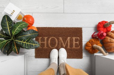 Balkabaklı ve fenerli kadın beyaz ahşap zeminde paspasın yanında duruyor.