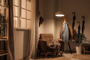 Koltuk, dekoratif ağaç, askı ve koridorun içinde parlayan lambalar.