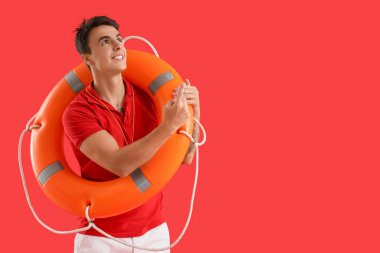 Kırmızı arka plandaki bir şeyi işaret eden halka şamandıralı bir erkek cankurtaran.