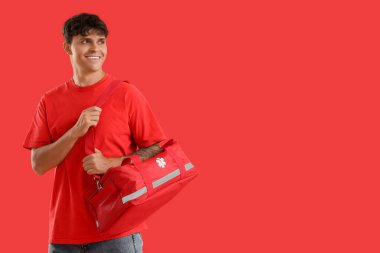 Kırmızı arka planda ilk yardım çantası olan genç adam.