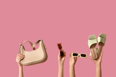 Farklı stil güneş gözlüklü, sandaletli ve pembe arka planda el çantalı kadın elleri.