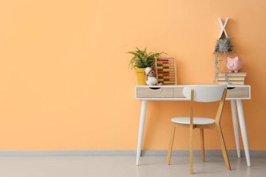 Kitaplı masa, abaküs ve çocuk odasındaki turuncu duvarın yanındaki bitkiler.