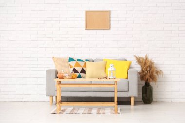 Rahat bir kanepe, vazoda otlar, sonbaharda oturma odasının içinde balkabağı ve fenerle dolu kahve masası.