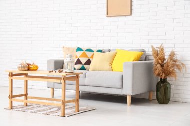 Rahat bir kanepe, vazoda otlar, sonbaharda oturma odasının içinde balkabağı ve fenerle dolu kahve masası.