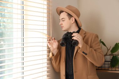 Ofiste pencerenin yanında dürbünü olan erkek dedektif.