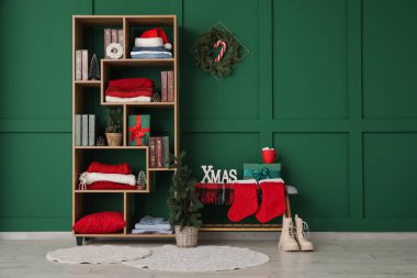 Kitaplarla dolu bir kitaplık, kışlık giysiler ve yeşil duvarın yanında Noel süsleri.