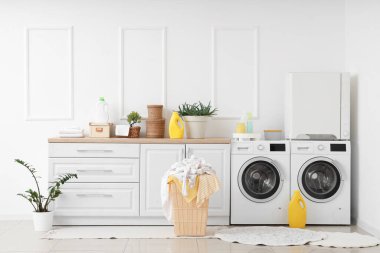 Çamaşır makinesi, tezgah, kurutucu ve sepet. Çamaşır odasının içinde giysiler var.