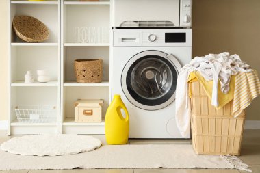 Çamaşır makinesi, kurutma makinesi, raf ünitesi ve çamaşır sepetinin içi çamaşır odasıyla dolu.