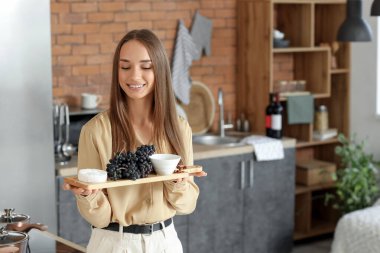 Mutfakta üzüm ve peynir taşıyan genç bir kadın.