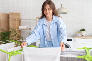 Çamaşır odasında kurutucuya temiz havlu asan genç bir kadın.