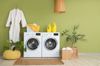 Çamaşır makinesi, sepeti ve bornozu olan bir çamaşırhane.