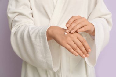 Genç bir kadın, leylak arka planına kozmetik krem sürüyor.