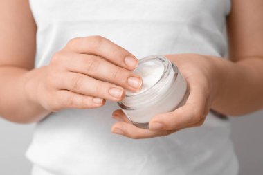 Gri arka planda kozmetik kremi kavanozu olan genç bir kadın.