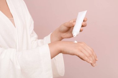 Genç bir kadın, leylak arka planına kozmetik krem sürüyor.