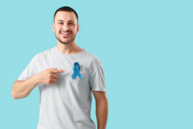 Genç adam arka plandaki mavi kurdeleyi işaret ediyor. Prostat kanseri farkındalığı