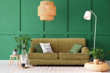 Konforlu kanepe, çiçekler ve yeşil duvarın yanındaki lamba.