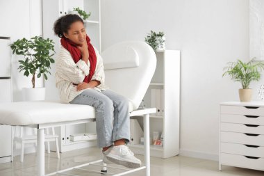 Klinikteki kanepede oturan boğazı ağrıyan Afro-Amerikalı kız.