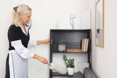 Orta yaşlı oda hizmetçisi otel odasında toz beziyle mobilya temizliyor.