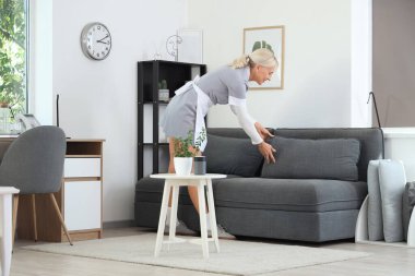 Orta yaşlı oda hizmetçisi otel odasındaki kanepede yastık ayarlıyor.