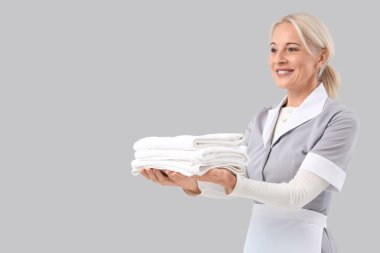 Gri arka planda bir yığın temiz havlusu olan orta yaşlı oda hizmetçisi