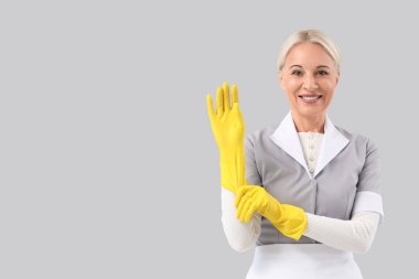 Orta yaşlı oda hizmetçisi gri arka plana lastik eldiven takıyor.