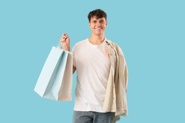 Mavi arka planda alışveriş torbaları olan yakışıklı bir genç.