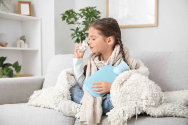 Hasta küçük kız sıcak su şişesiyle evdeki kanepede hapşırıyor.