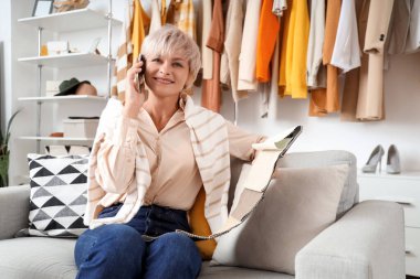 Kumaş örnekleriyle mutlu bir kadın stilisti cep telefonuyla stüdyoda şık kıyafetlere karşı konuşuyor.