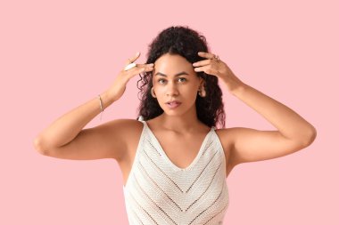 Pembe arka planda şık mücevherleri olan güzel bir Afro-Amerikalı kadın.