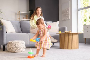 Sevimli bebek, oyuncaklarla yürümeyi öğreniyor ve annesi evde.