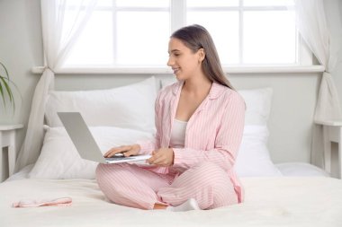 Pijamalı genç bir kadın evde dizüstü bilgisayar kullanıyor.