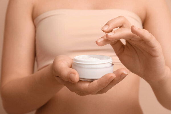 Молодая женщина с банкой косметического крема на коричневом фоне, крупным планом