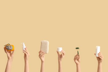 Yüzü çizilmiş balkabağı tutan kadın eller, banyo süngeri, şişeler ve bej arka planda kozmetik ürünler kavanozu