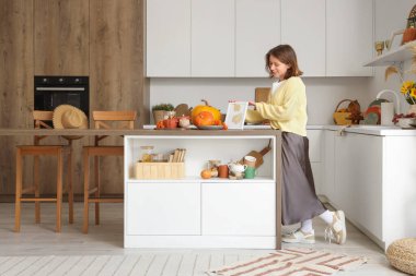 Balkabaklarıyla, böğürtlenleriyle ve sonbahar süslemeleriyle aydınlık mutfakta güzel bir kadın.