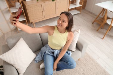 Cep telefonlu genç bir kadın evdeki kanepede selfie çekiyor.