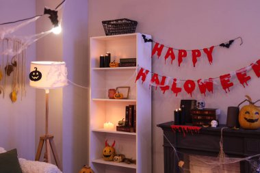 İçinde şömine, yanan mumlar, balkabakları ve Cadılar Bayramı süslemeleri olan karanlık bir oturma odası.