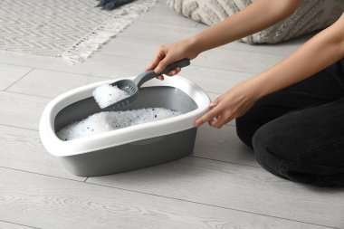 Kadın oturma odasında kedi için çöp kutusunu temizliyor.