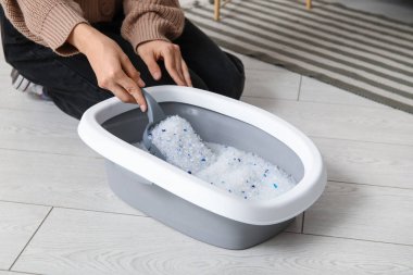 Kedi için kepçe temizleme kutusu olan bir kadın oturma odasında yerde yatıyor.