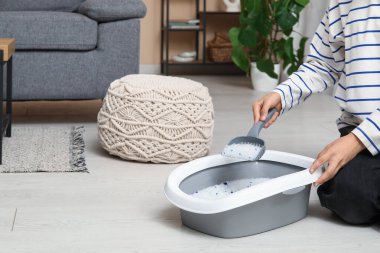 Kadın odada kedi için çöp kutusunu temizliyor.