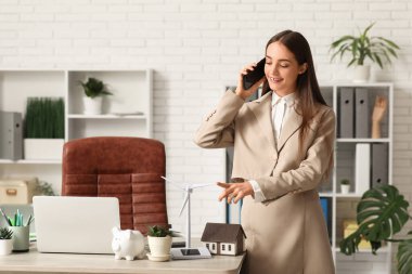 Ofiste rüzgar türbini modeliyle cep telefonuyla konuşan kadın mühendis.