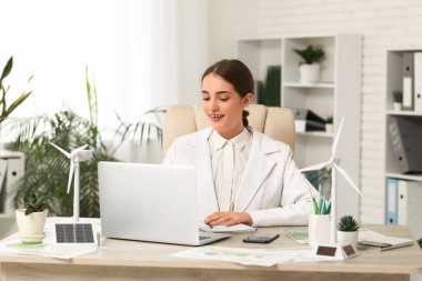 Ofisteki masada dizüstü bilgisayar ve rüzgar türbinleriyle çalışan kadın mühendis.