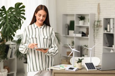 Ofisteki masada tablet bilgisayar ve rüzgar türbini modelleriyle çalışan kadın mühendis.