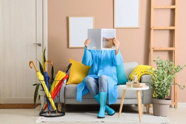 Koridordaki kanepede yağmurluk okuyan kadın.