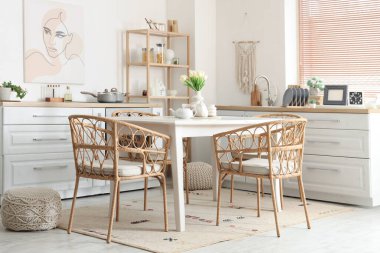 Ahşap yemek masası, rattan koltuklar ve şık mutfağın içindeki beyaz tezgahlar.