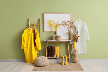 Koridorun içinde yağmurluklar, masa ve çizmeler var.