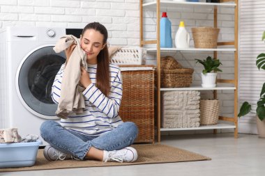 Güzel, genç, mutlu, temiz çamaşırları olan bir kadın evde oturuyor.