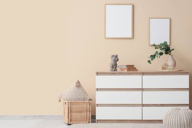 İçinde lamba olan çekmeceler, yastıklı sepet ve bej duvarın yanındaki puf.