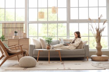 Genç bir kadın şık bir oturma odasında dizüstü bilgisayarla sohbet ediyor.