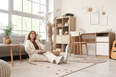 Oturma odasındaki kanepenin yanında dizüstü bilgisayarla sohbet eden genç bir kadın.