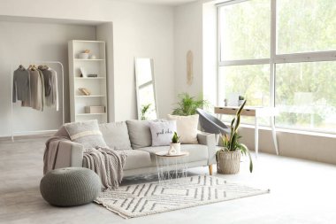 Gri kanepeli, sehpalı, çiçekli ve pencereli aydınlık oturma odasının içi.